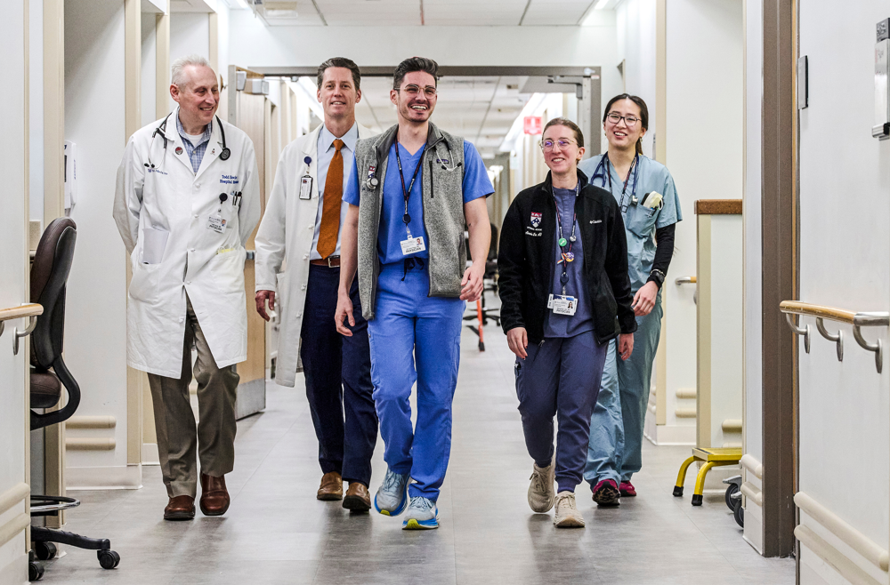 From left: Todd Hecht, MD, and Hospital Medicine chief S. Ryan Greysen, MD, and colleagues in scrubs walk down a hospital hallway.
